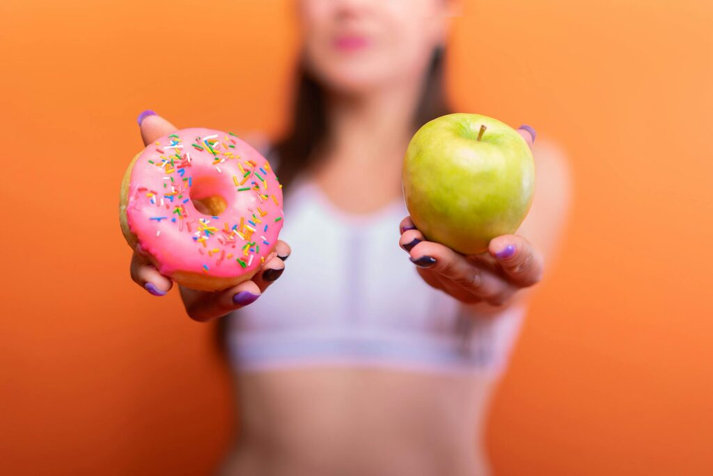 una chica con un donuts en la mano y con una manzana en la otra