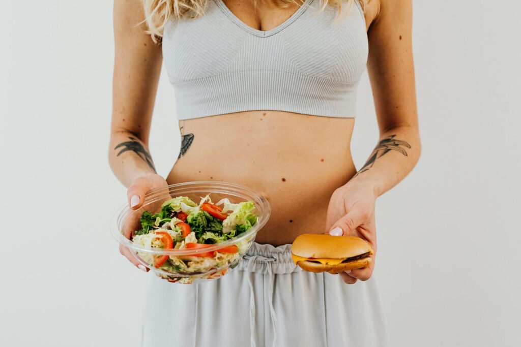 una chica con un bol de ensalada en una mano y con una hamburguesa en la otra
