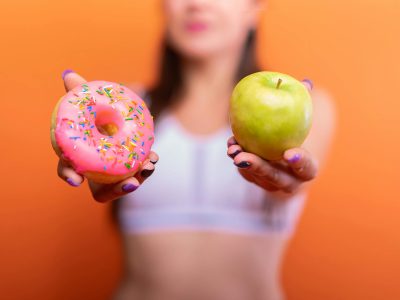 una chica con un donuts en una mano y una manzana en la otra mano
